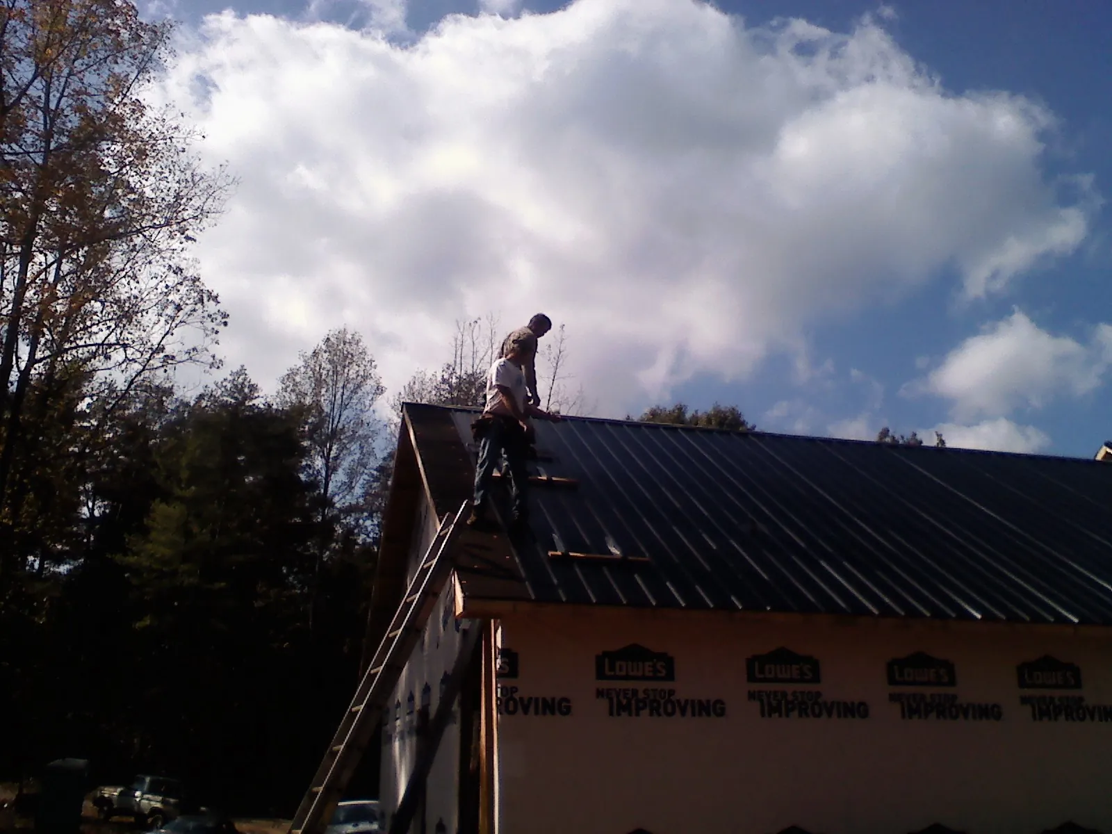 Roofer fastening dark metal panels high against a cloudy sky, from a Roof Inspection job in Perryville